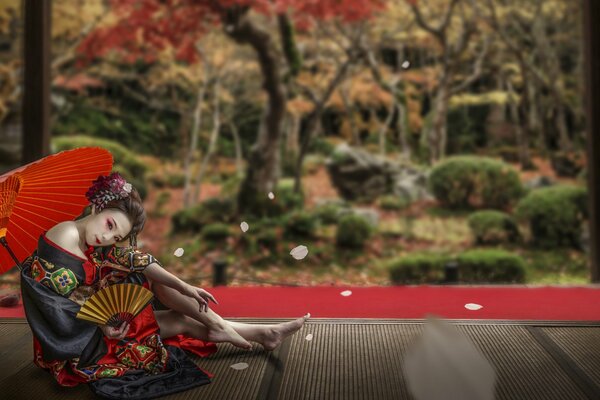 A girl in an Asian outfit with an umbrella is sitting in a gazebo against the background of a forest