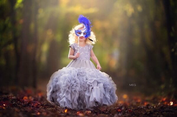 A little girl in a ball gown with a blue mask