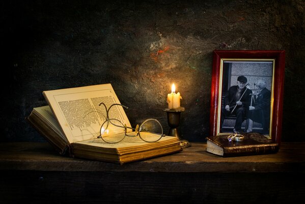 Ein Buch mit Brille auf einem Tisch neben einer Kerze und einem gerahmten Foto