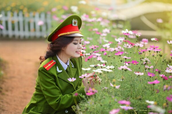 Una chica con uniforme militar se sienta cerca de un campo de flores