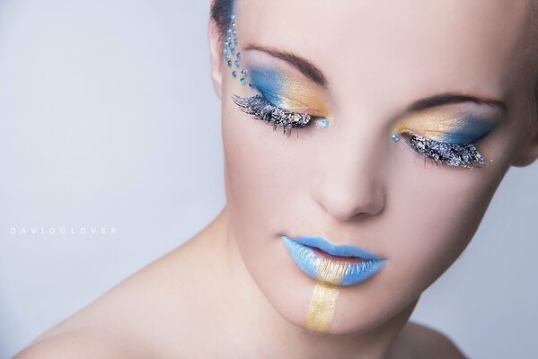 A girl s face looking down with beautiful eye and lip makeup in a blue-yellowish shade