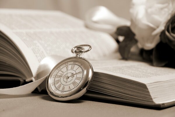 Un gros livre ouvert et une petite horloge appuyée contre elle