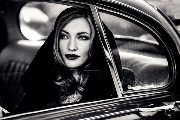 A girl in a black hood looks out of the window of a retro car