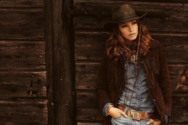 Красивая девушка в ковбойской шляпе на фоне деревянной стены