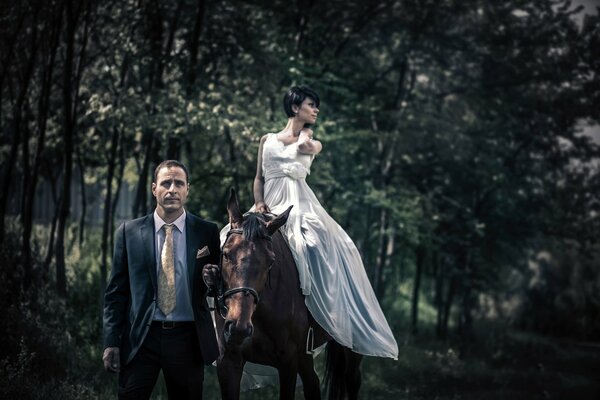 A man in a suit leads a horse with a girl on horseback , a stylish couple