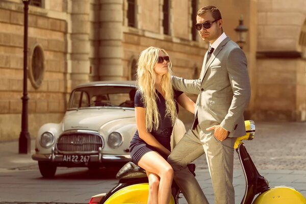 Verano en Copenhague, pareja en trajes de moda con un ciclomotor amarillo y un auto Vintage
