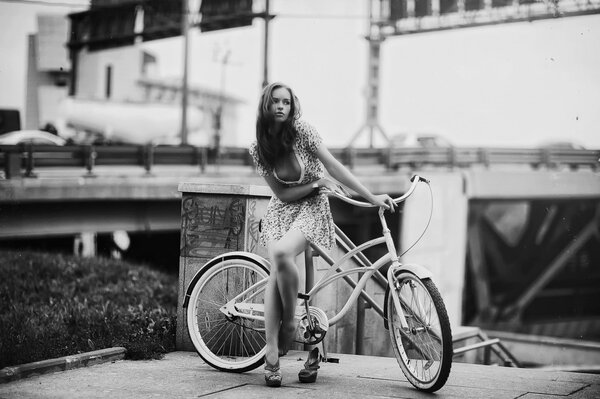 Photo in retro style, a girl in a short dress with a bicycle on the background of a road junction