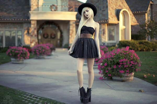 A girl in a black dress poses against the background of a house