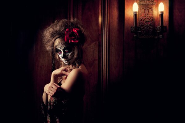 Una chica con la cara pintada para el día de los muertos. La imagen complementa la flor roja en el cabello