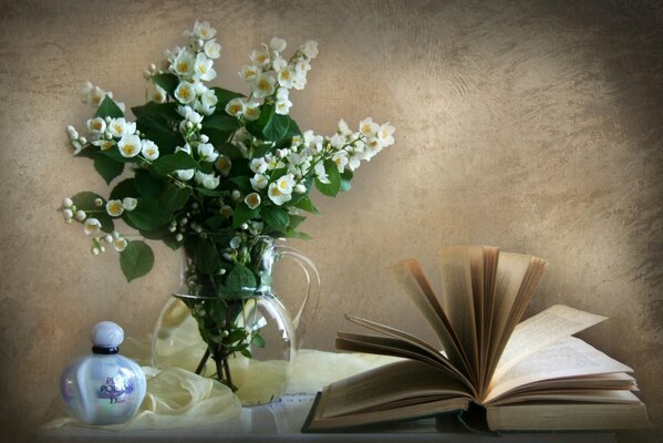 Духи книга и жасмин в вазе на столе