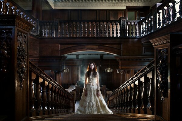 Chica en un vestido blanco en las escaleras en una casa antigua