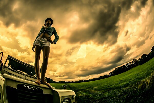 A girl is standing on a car in a field