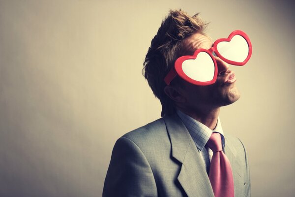 Un gars en costume et avec des lunettes en forme de coeur