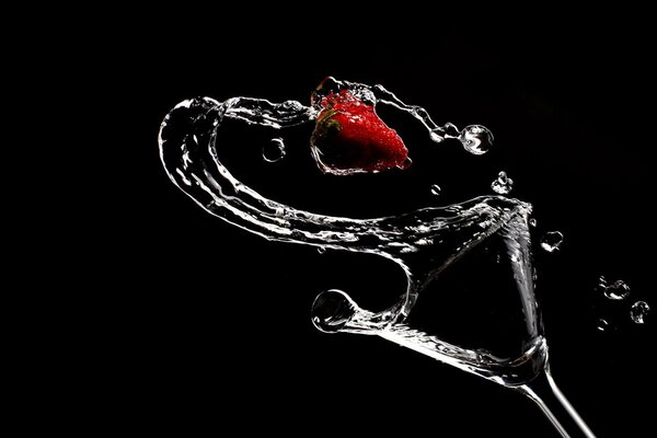 Fino, das aus einem Glas und roten Erdbeeren auf schwarzem Hintergrund abgefüllt wird