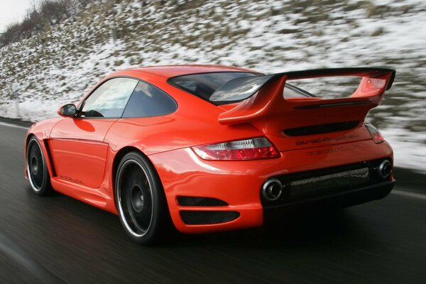 A red car is driving along a snowy road