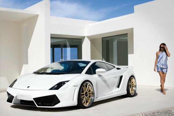 A beautiful girl is standing at the house next to a lamborghini