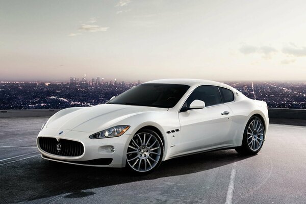 Against the background of a distant evening city - a white Maserati supercar