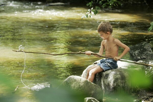 A boy is fishing on the river with a fishing rod