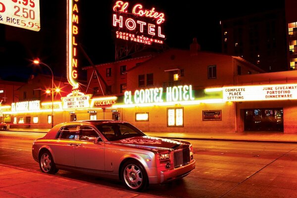 Rolls royce en medio de un anuncio de neón y una ciudad nocturna