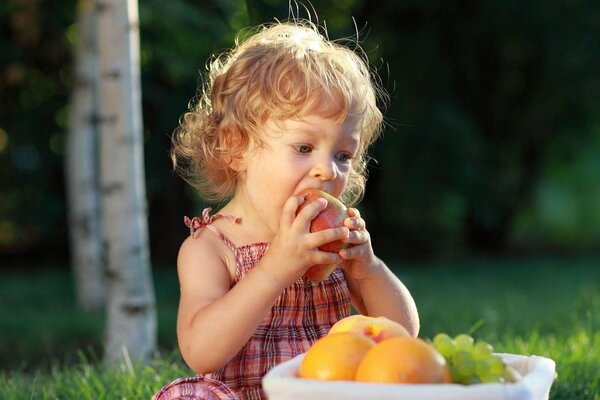 A girl eats an apple from a fruit basket