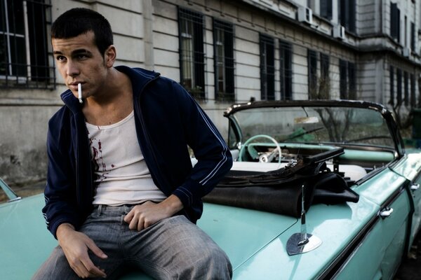 Mario Casas is sitting on the hood of a car