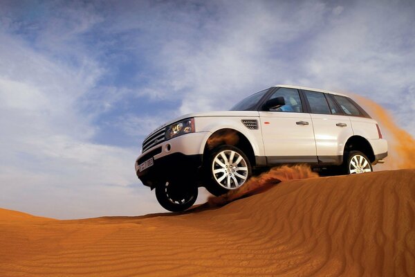 A white jeep jumps over a dune of sand