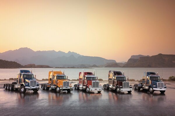 Пять грузовиков стоят на фоне залива и гор