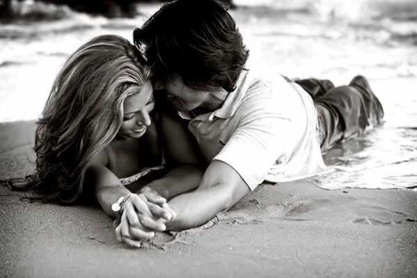 A guy and a girl are lying on the sand. Black and white image