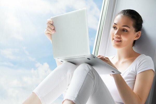 A pretty brunette with a laptop on the background of a window