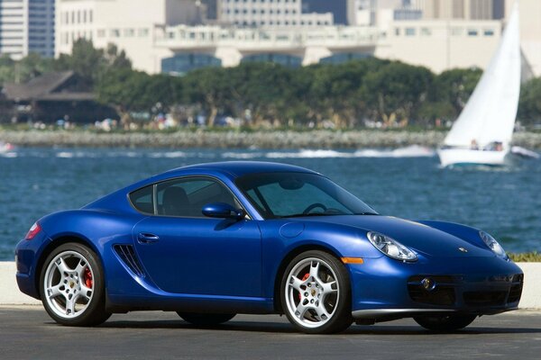 Blue porsche on the background of water and a sailboat