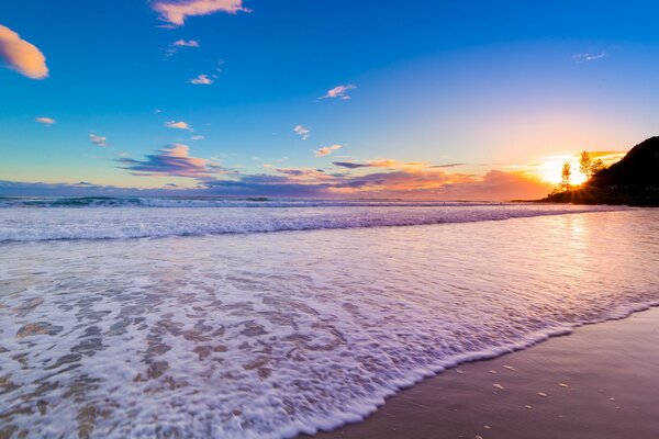 Пенная волна катящаяся по морскому песку на закате