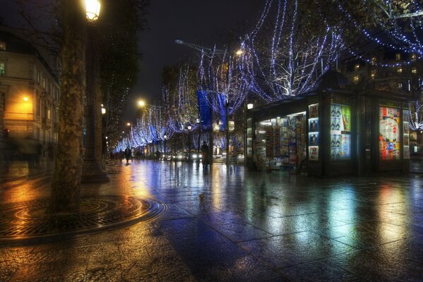 Una ciudad nocturna con asfalto mojado después de la lluvia, en la que se reflejan las luces de escaparates, ventanas y linternas