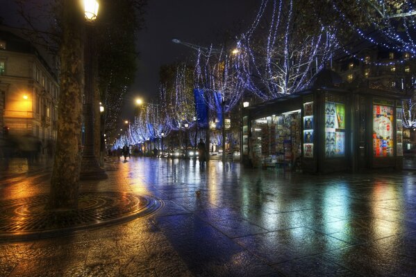 Nocne miasto z mokrym asfaltem po deszczu, w którym odbijają się światła witryn sklepowych, okien i latarni