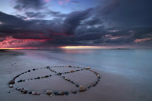 A sign made of stones on the sand on the seashore at sunset