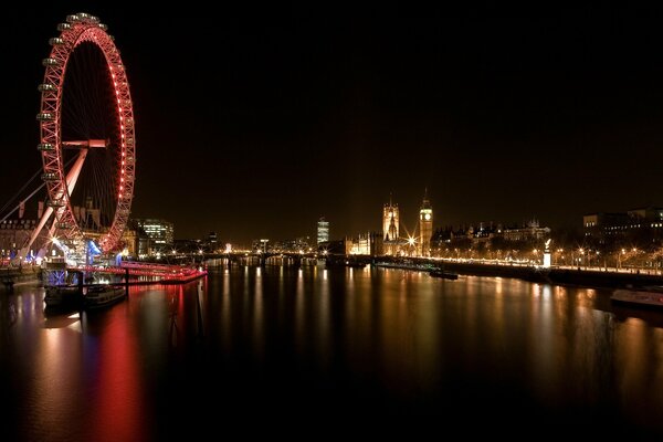 The Ferris wheel is reflected in the dark waters of the river. London