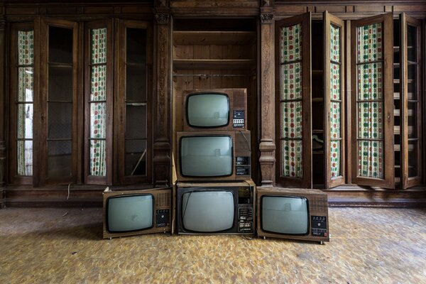 Eine Pyramide aus alten Fernsehern vor dem Hintergrund von Holzschränken