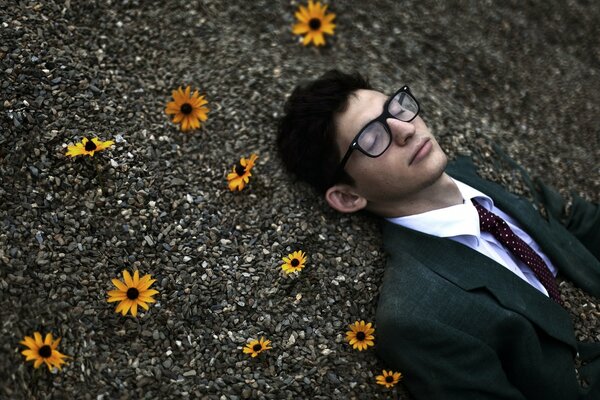 Hombre en traje yace en piedras con flores