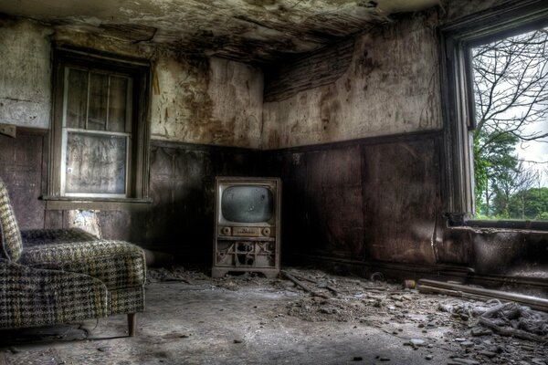 A dirty abandoned room with an armchair and a TV