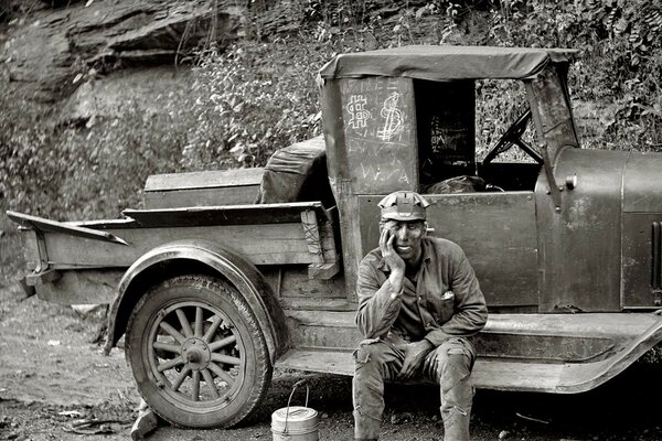Ein alter Lastwagen, und ein Mann sitzt vor der Haustür und stützt seinen Kopf