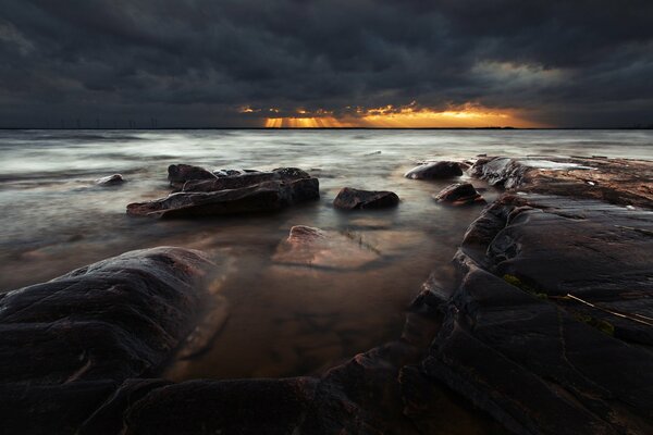 Темный закат у каменного морского пляжа