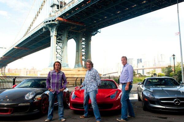 Three sports cars and three men are standing under the bridge