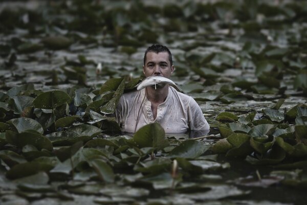 Ein Mann mit einem Fisch im Mund steht im Teich