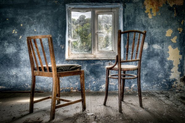 Dos sillas cerca de una ventana con telarañas en una habitación abandonada