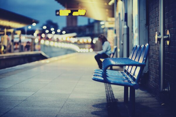 Niña sentada en una silla por la noche en la estación de tren de la ciudad