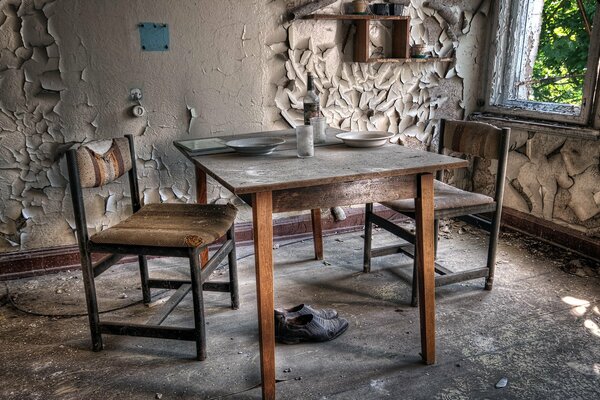 There is an old table and chairs against the background of a peeling kitchen wall