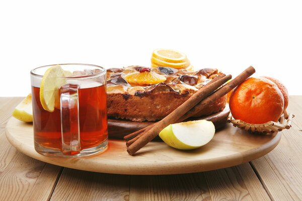 Чашка чая, пирог, коричные палочки, яблоки и апельсины на подносе