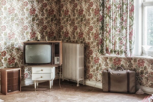 Habitación con papel tapiz de flores. Televisión y maleta