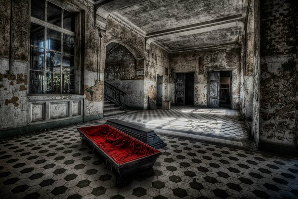 An open coffin lined with red silk fabric standing on the floor of an old abandoned room