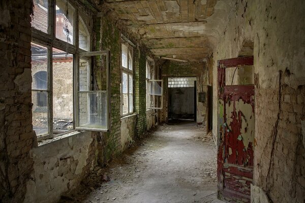 Un pasillo en ruinas con ventanas en relieve y puertas deshilachadas