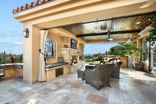 A veranda under the roof with armchairs and a fireplace